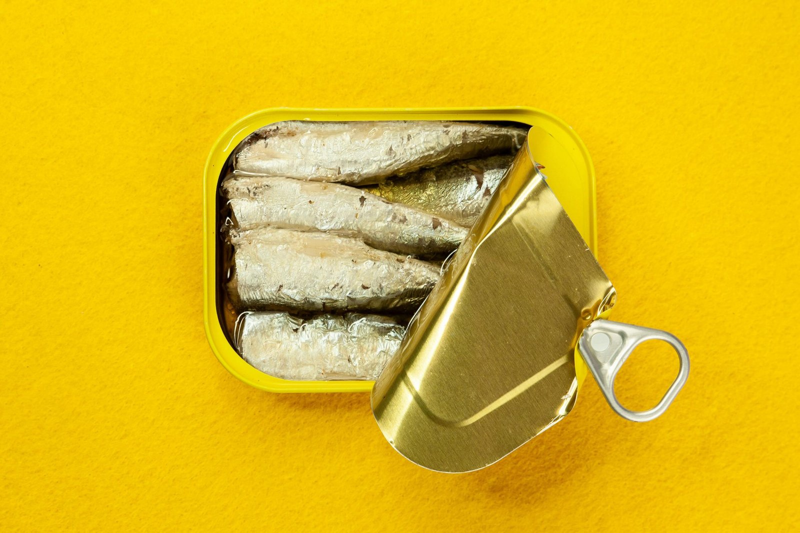 Freshly opened sardine can displayed against a bold yellow background, highlighting its contrast.